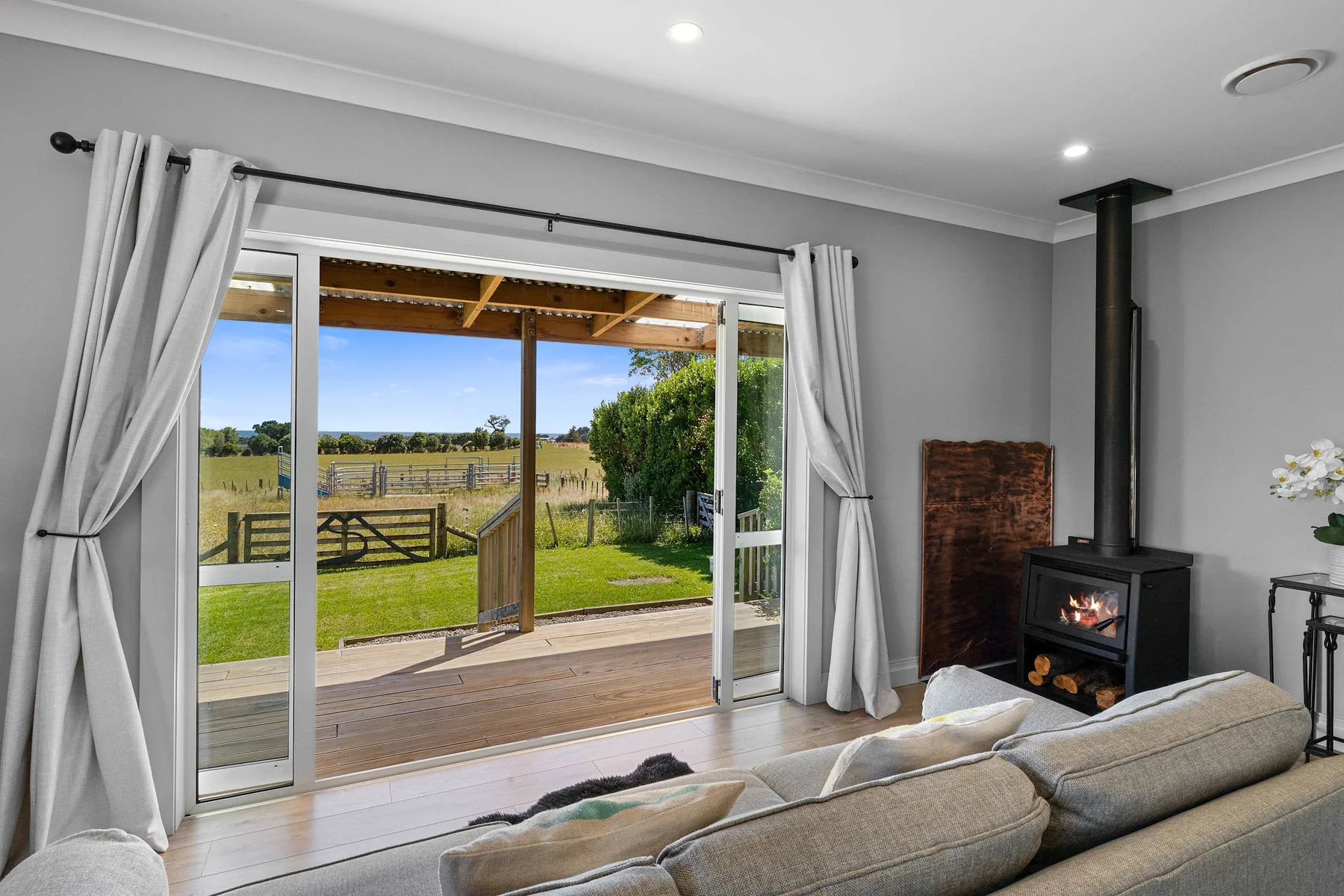 A living room opens onto a deck and a grassy fenced landscape.