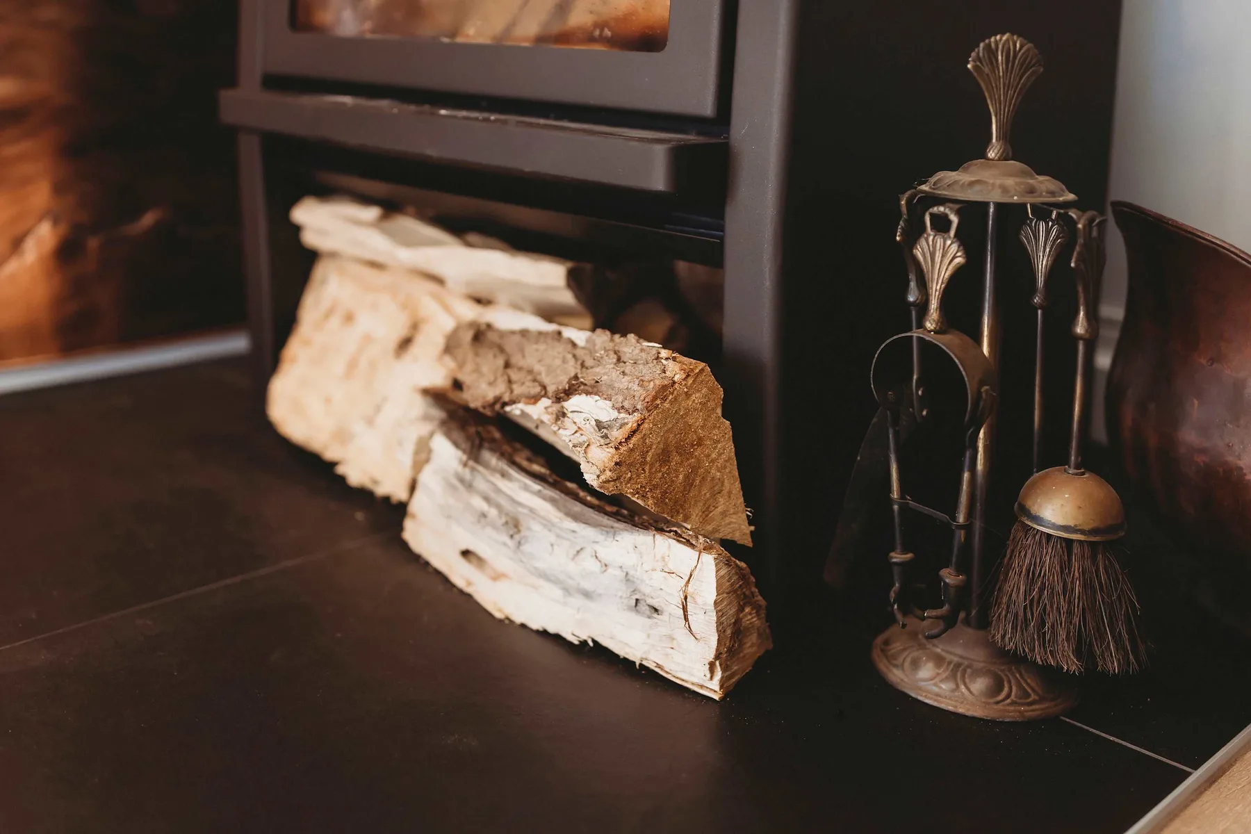 A fireplace hearth with stacked firewood and dark metal fireplace tools.