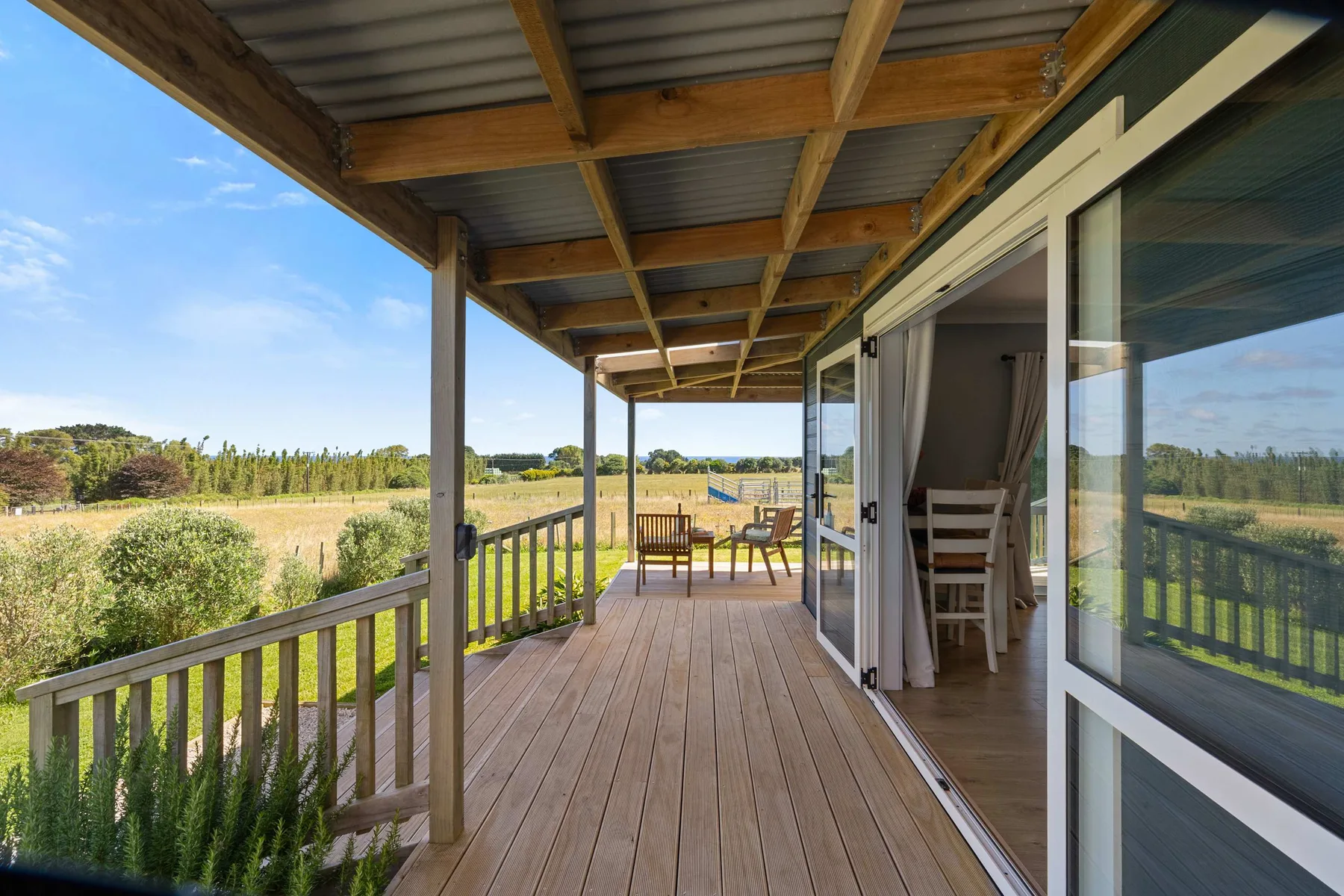 A covered wooden deck with outdoor seating overlooks an open grassy landscape.
