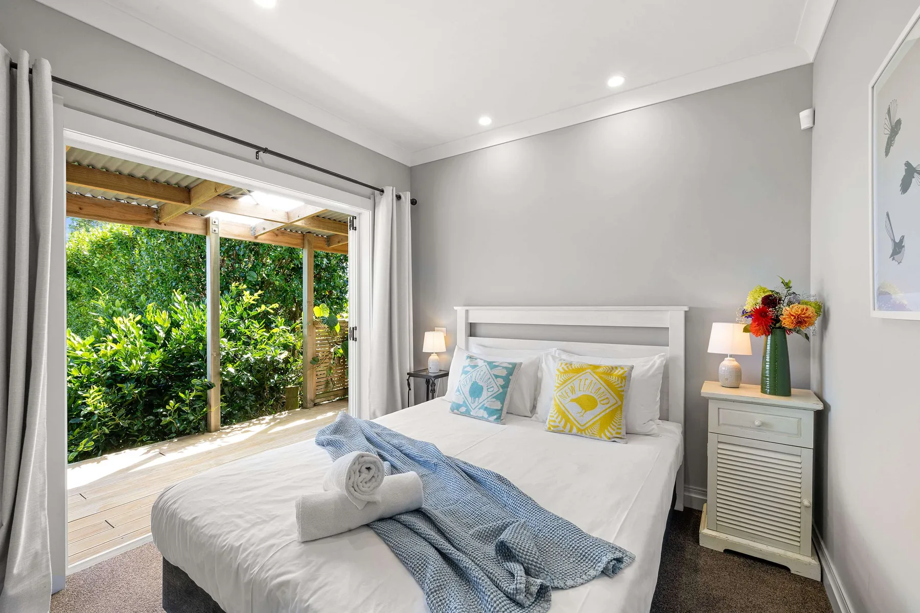 A bedroom with white bedding opens onto a garden patio.