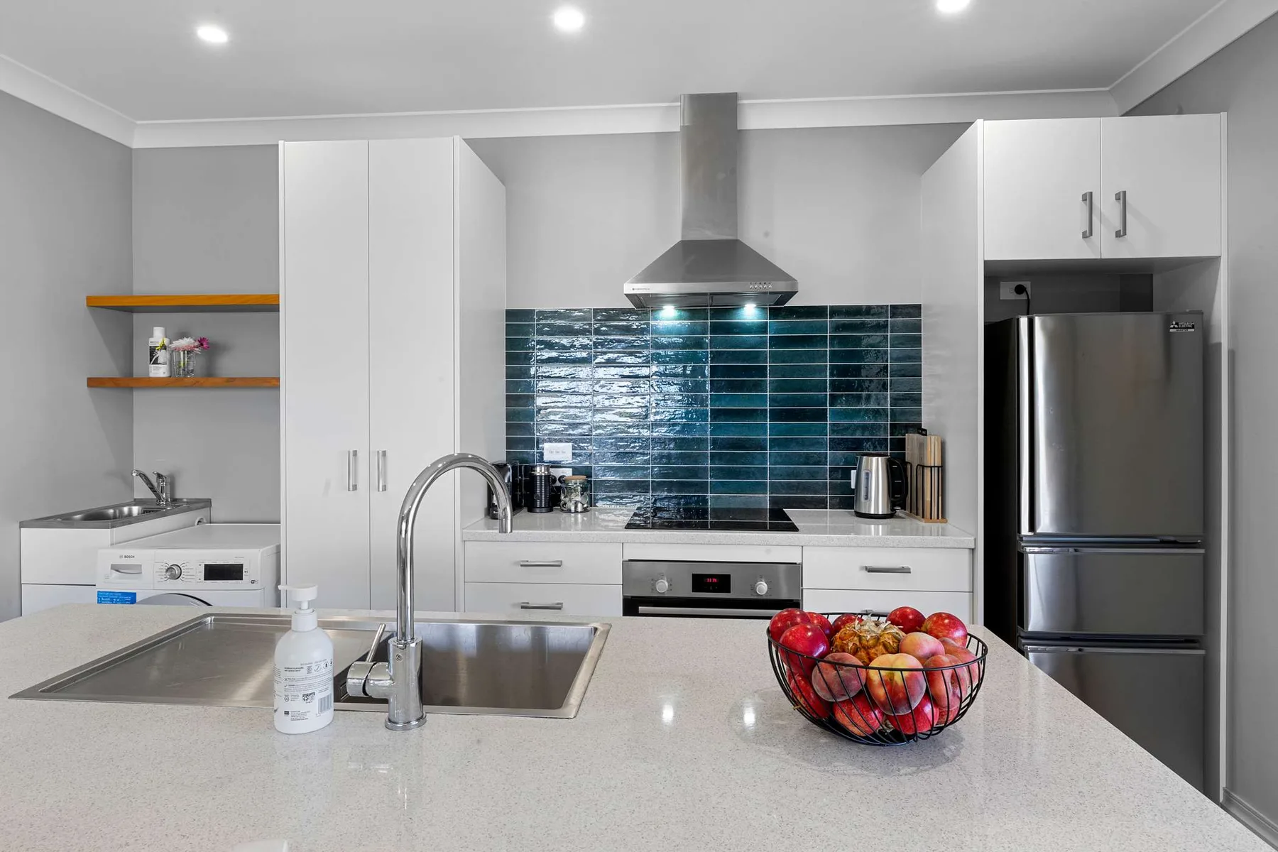 Una cocina moderna con una isla amplia, electrodomésticos de acero inoxidable y un salpicadero de azulejos oscuros.