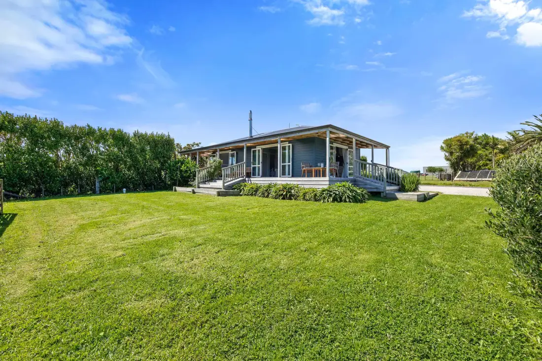 A single-story house with a deck sits beyond a broad green lawn.