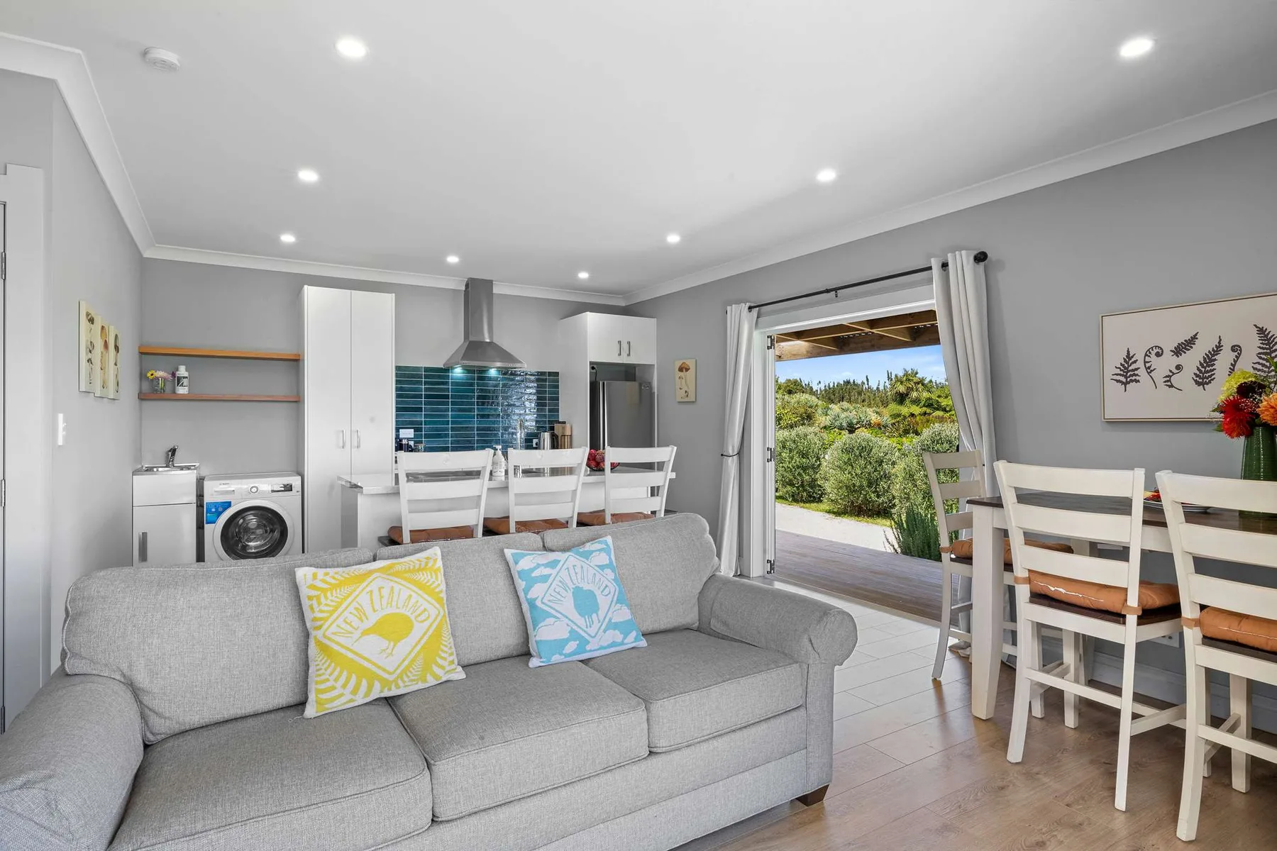 A bright living area with a gray sofa, dining table, and open kitchen.