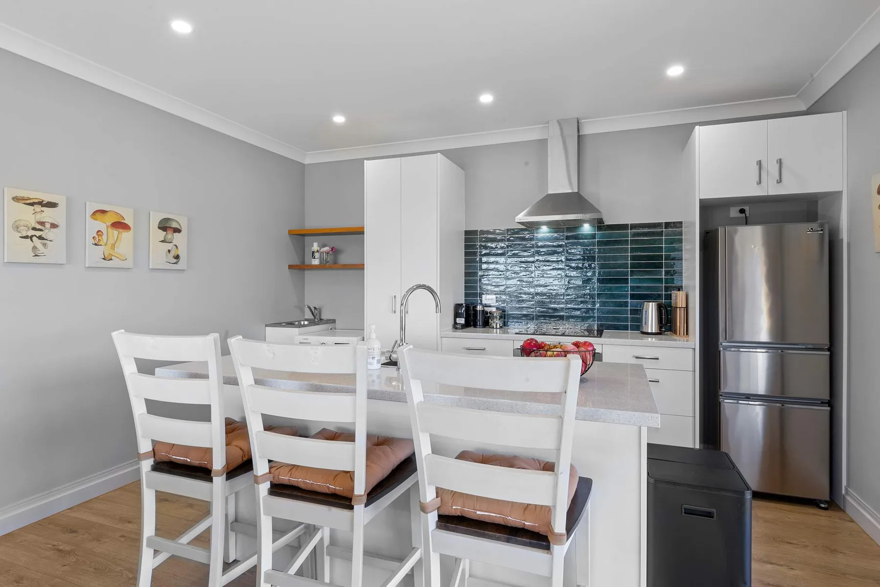 Una cocina luminosa con comedor, asientos blancos y salpicadero de azulejos oscuros.