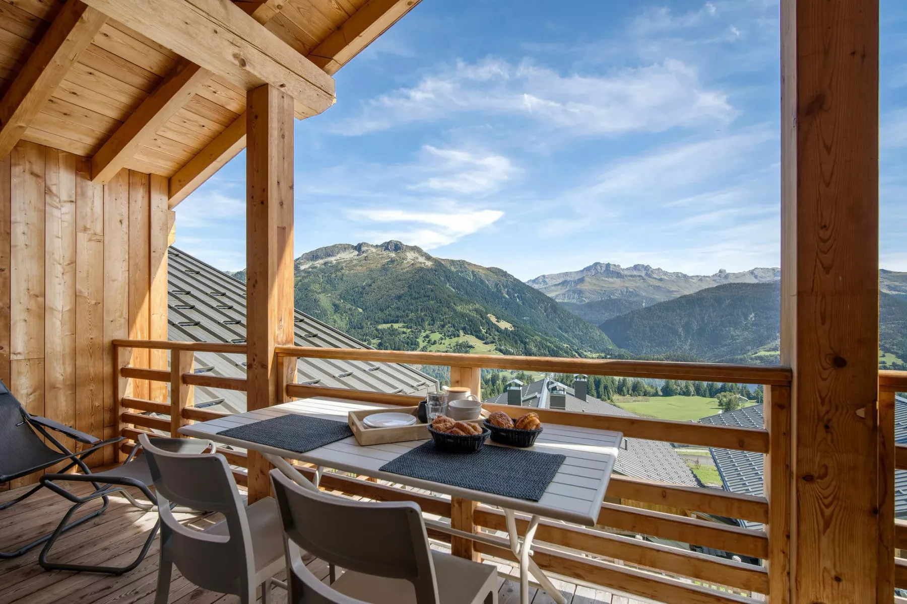 Una zona de comedor en un balcón de madera da a un valle montañoso.