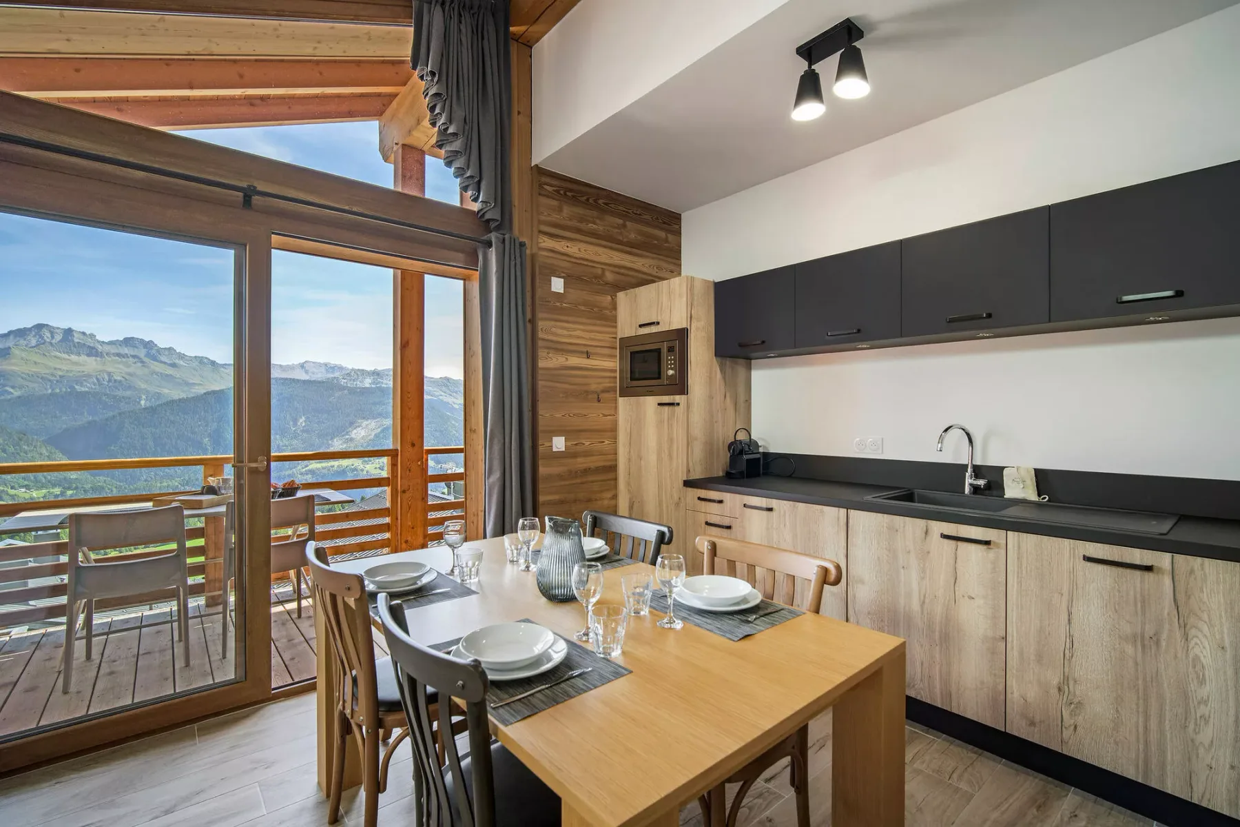 Comedor junto a una cocina compacta, con grandes ventanales y vistas a las montañas.