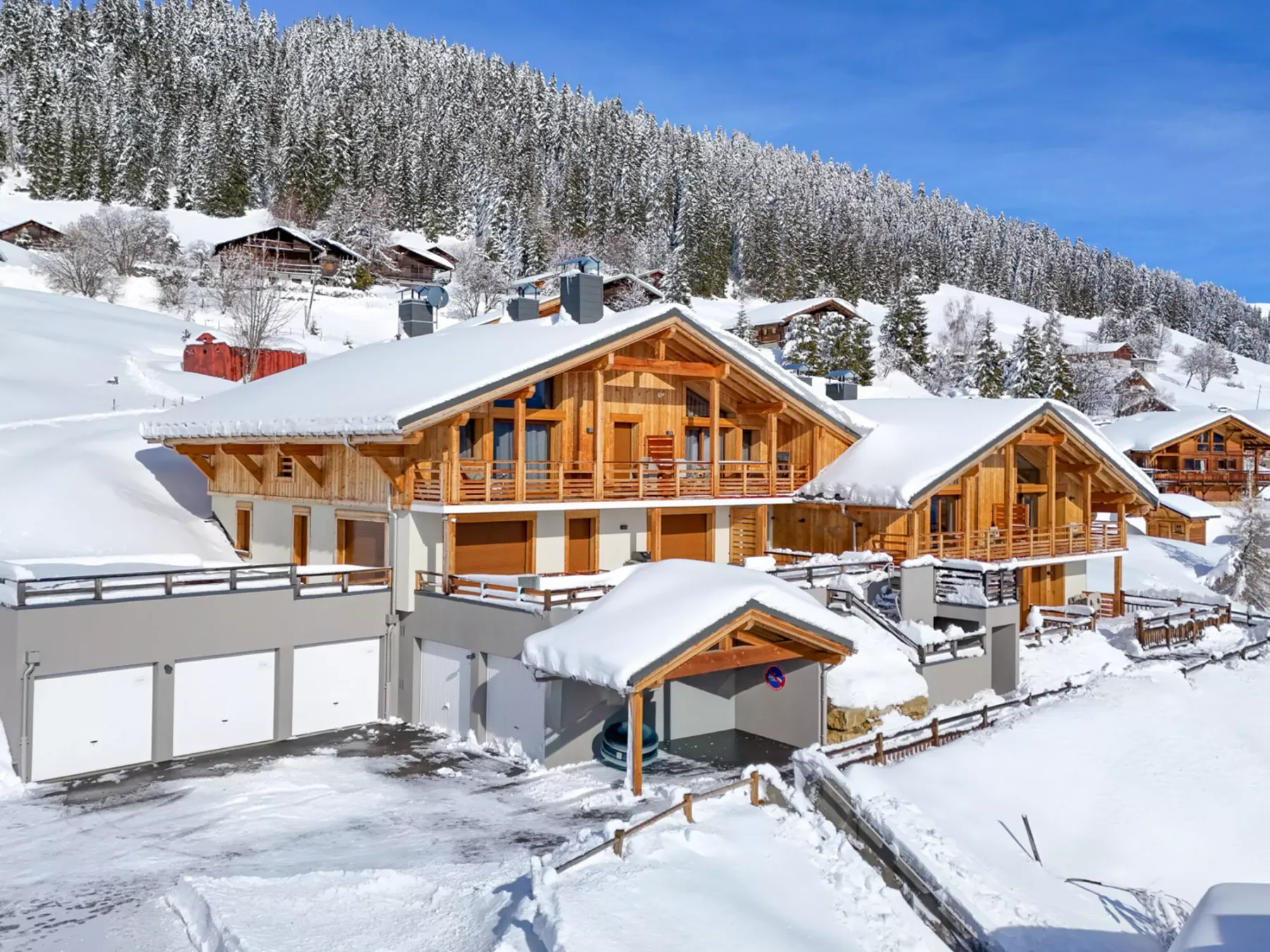 Chalés de madera cubiertos de nieve se encuentran bajo una montaña boscosa y un cielo despejado.