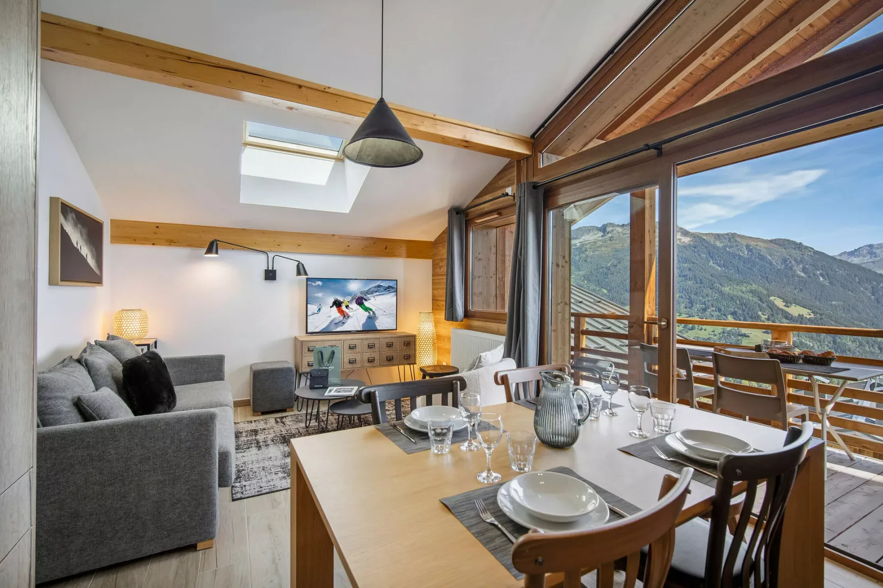 Una zona de comedor y estar se abre a un balcón con vistas a las montañas.