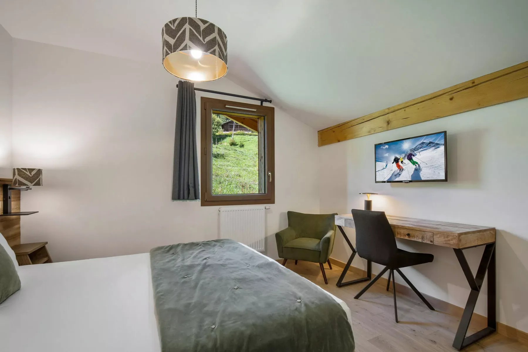 Un dormitorio con cama, escritorio, asientos y una ventana con vistas a la vegetación.