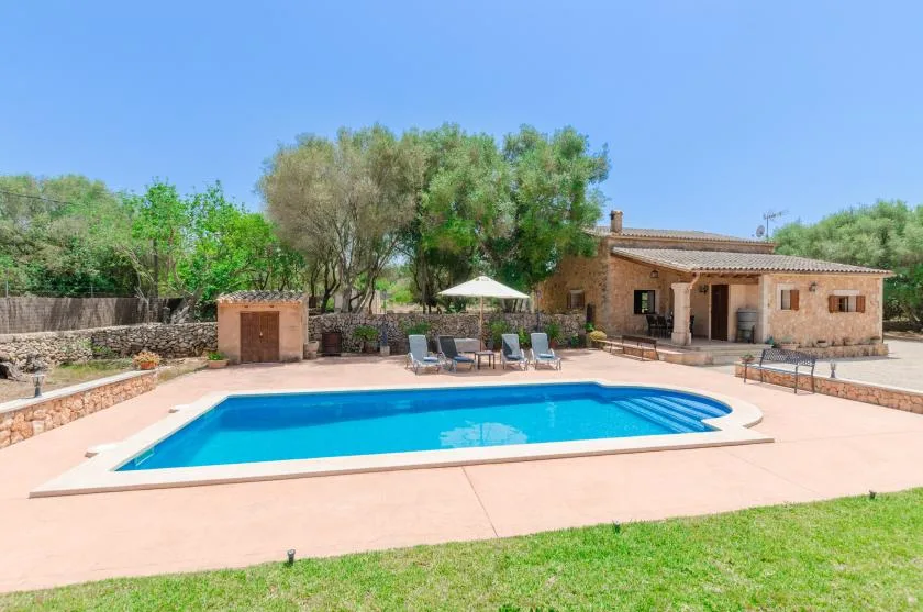 An outdoor swimming pool sits beside a stone building and green lawn.