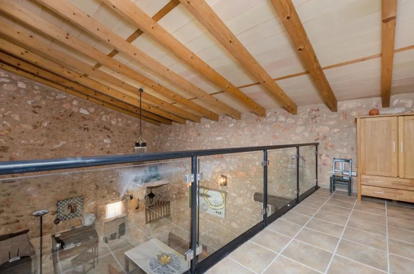 A tiled upper-level area overlooks a stone-walled room through a glass railing.