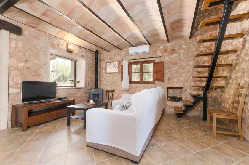 A stone-walled living room with white seating and a wooden staircase.