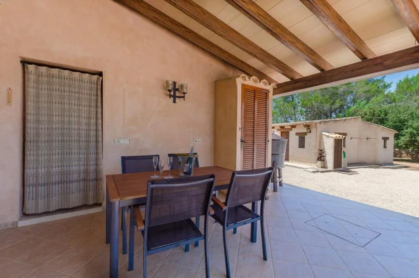 A covered patio has a dining table and seating beneath exposed wooden beams.
