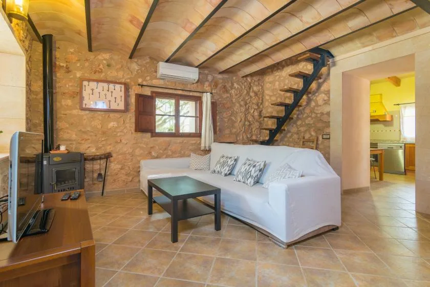 A rustic living room with white seating, a wood stove, and a staircase.