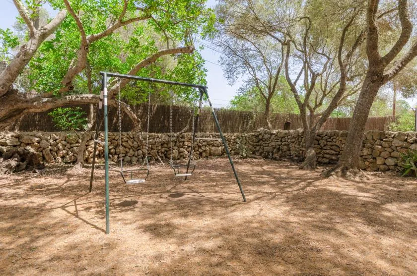 A shaded outdoor play area with a swing set beside a low stone wall.