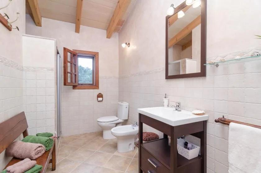 A tiled bathroom with a sink vanity, toilet, and window.