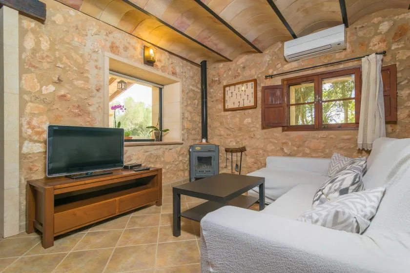 A stone-walled living room with white seating and a television.