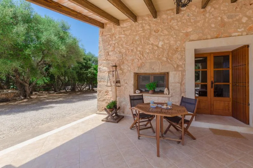 A covered patio with a dining table and chairs beside a stone exterior wall.