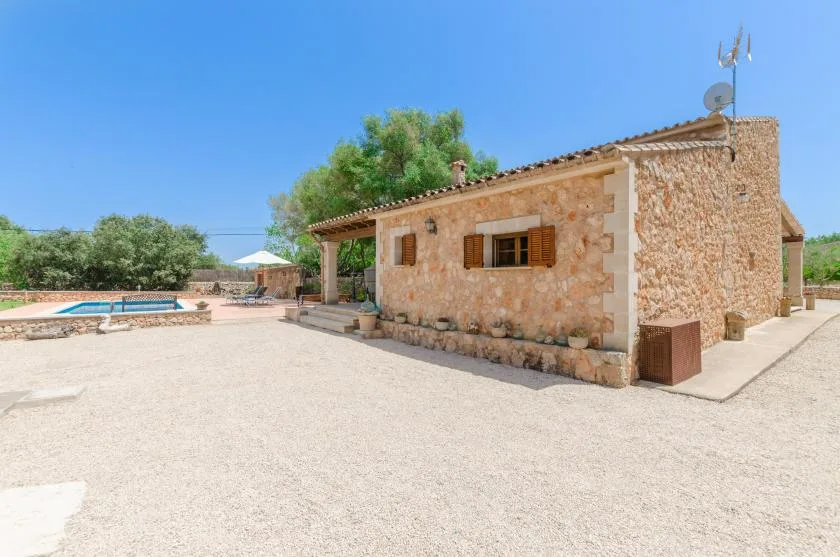 A stone house stands beside an open courtyard and a swimming pool.
