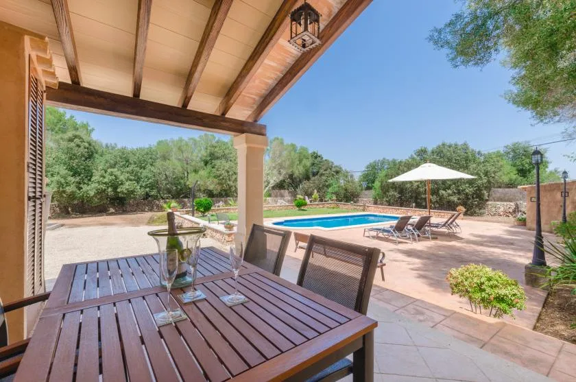 A covered patio with outdoor seating overlooks a swimming pool and garden.