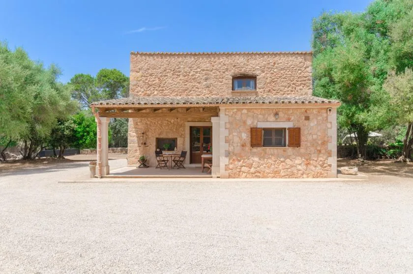 A stone house with a covered patio stands beside a broad gravel yard.