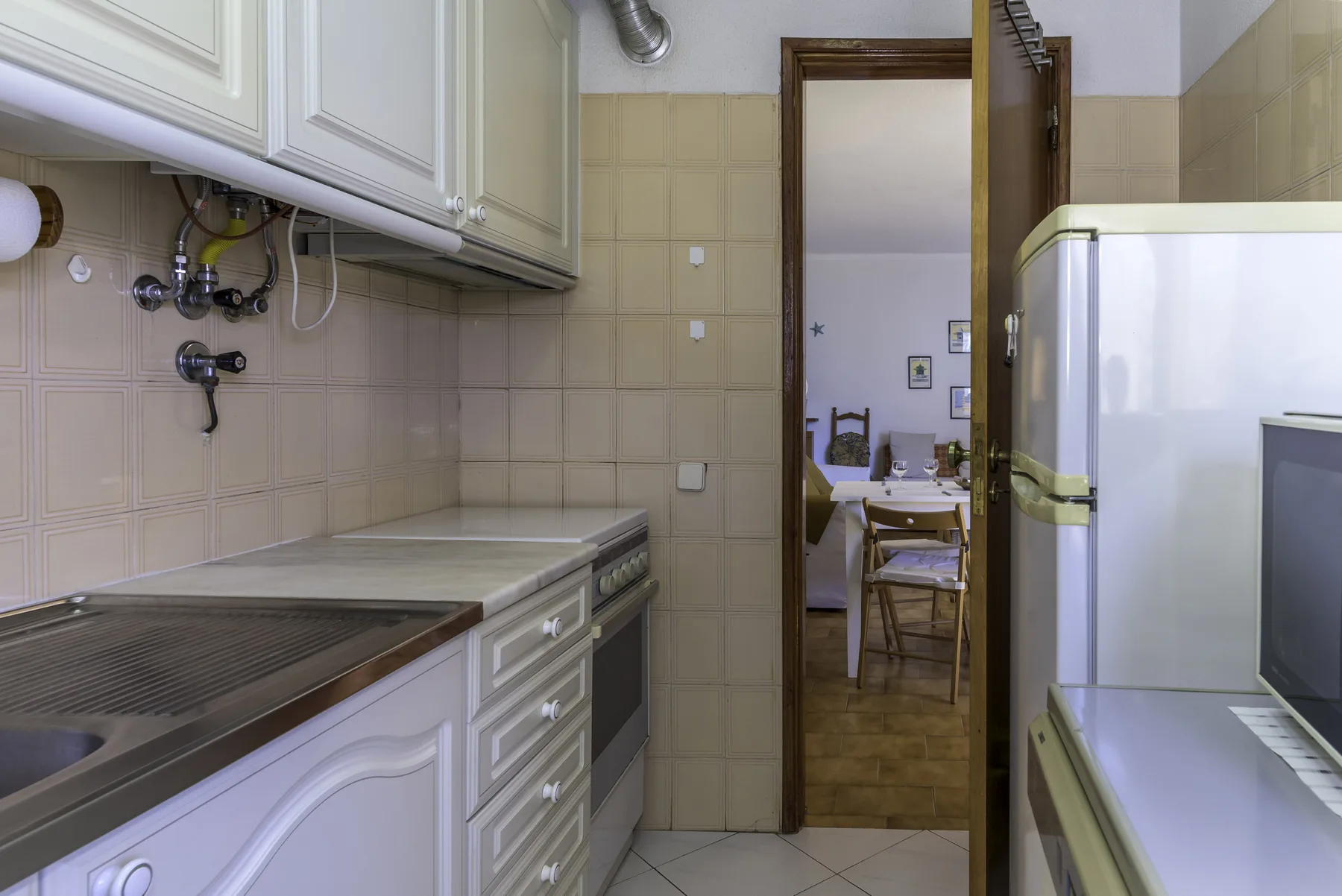 A tiled kitchen with cabinets and a dining table visible through the doorway.