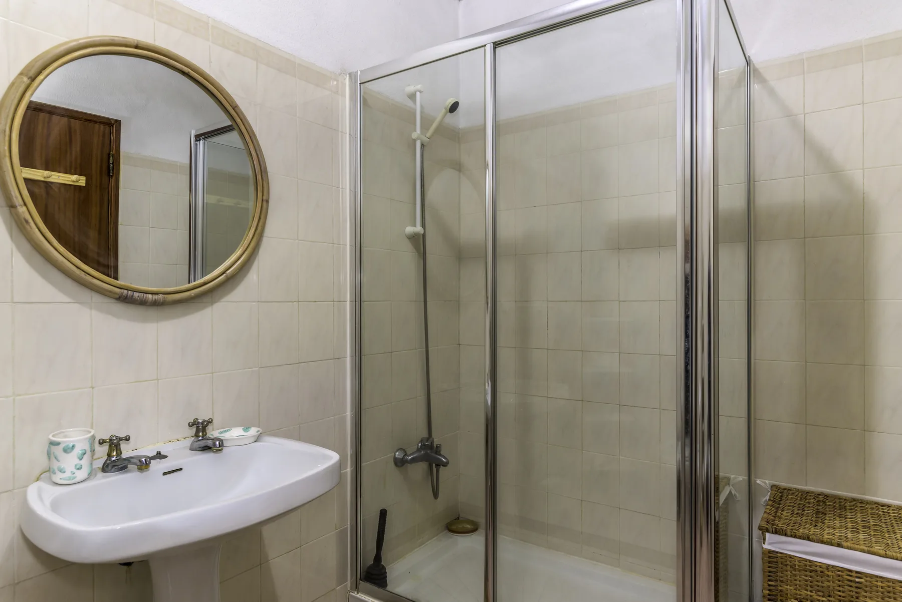 A tiled bathroom with a sink, round mirror, and glass-enclosed shower.