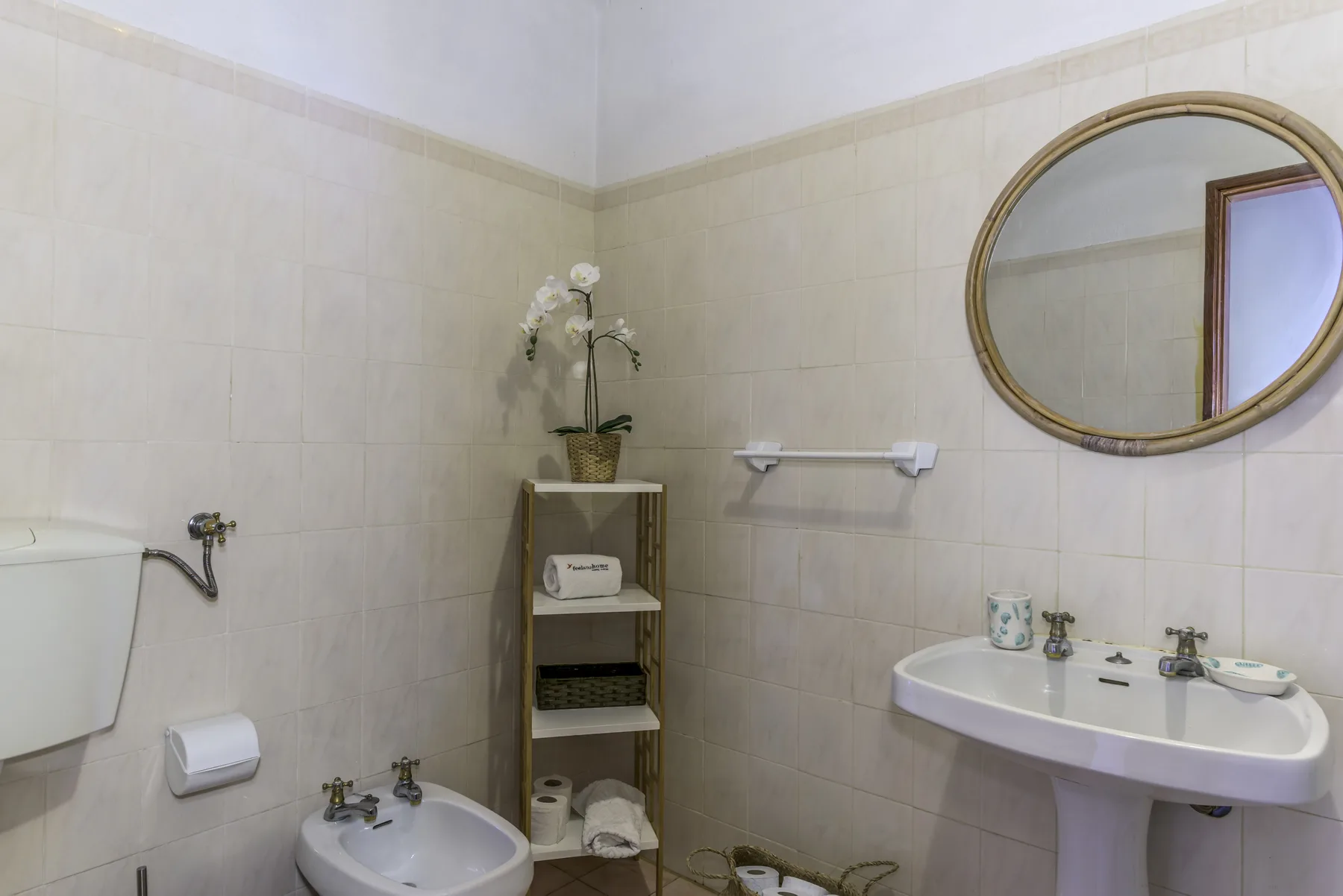 A tiled bathroom with a sink, toilet, and round wall mirror.