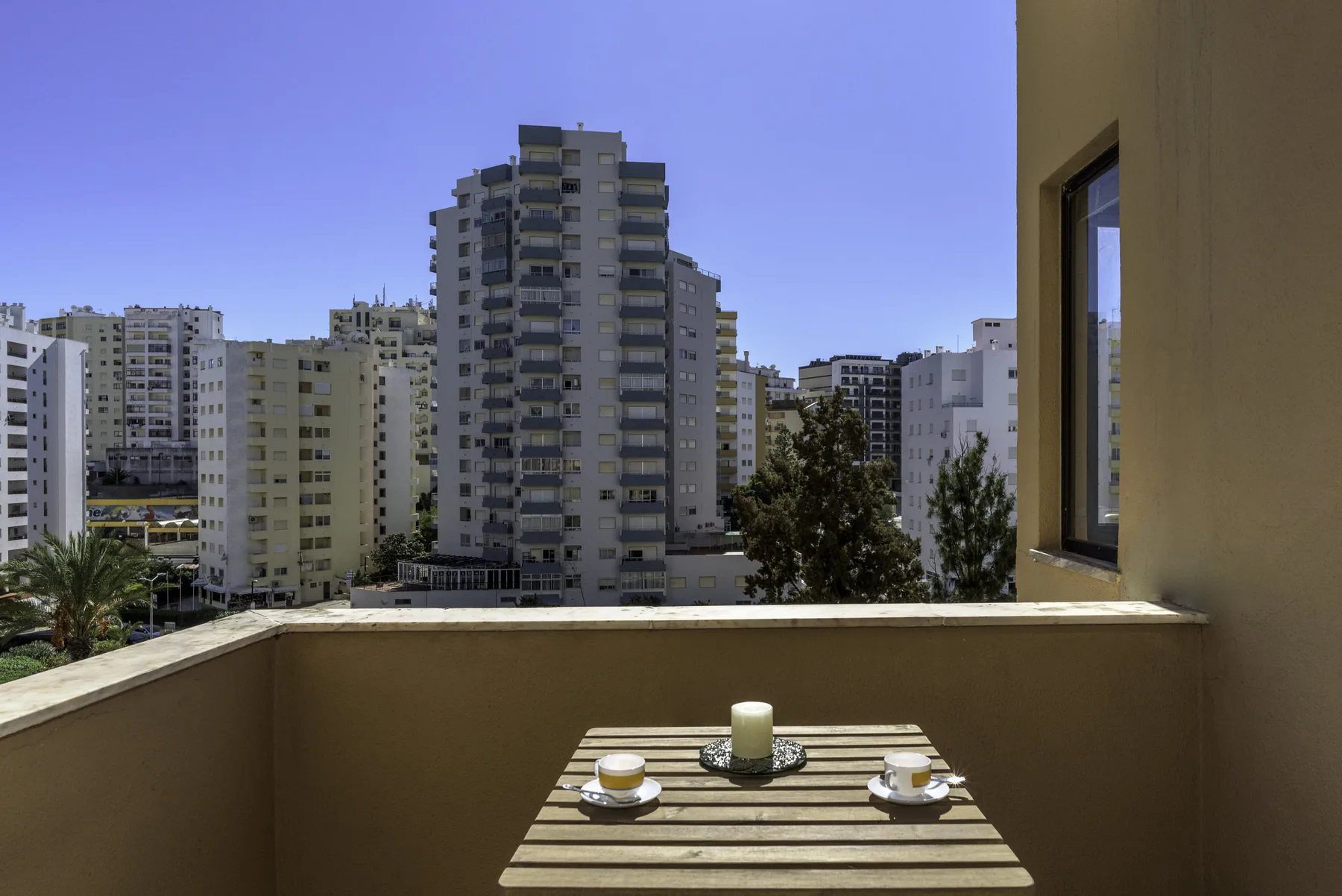 A balcony table with cups overlooks nearby apartment buildings.