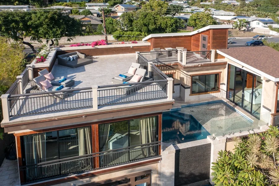 A modern rooftop terrace with lounge seating overlooks a swimming pool and nearby homes.