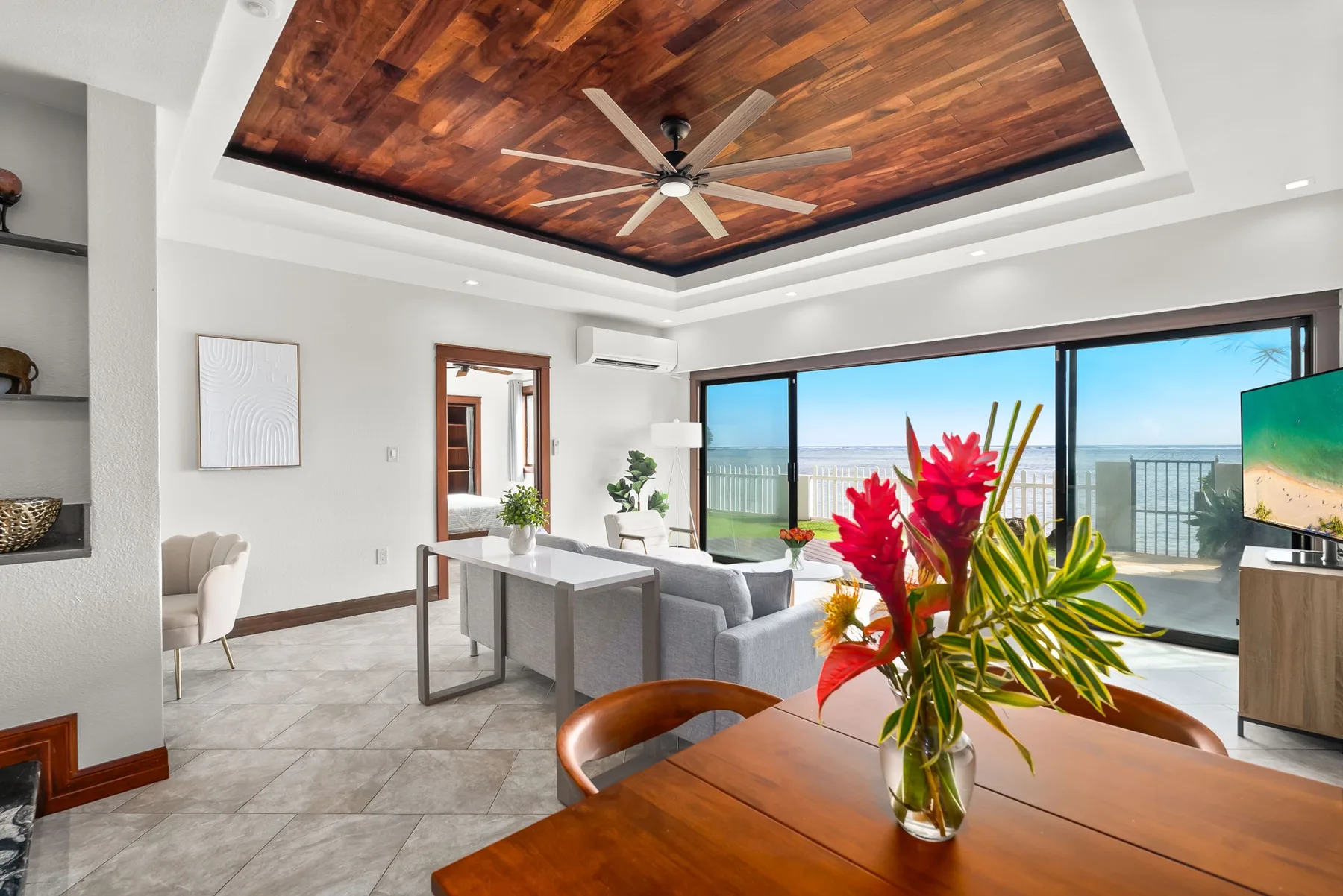 A bright living and dining area opens onto a balcony with a coastal view.