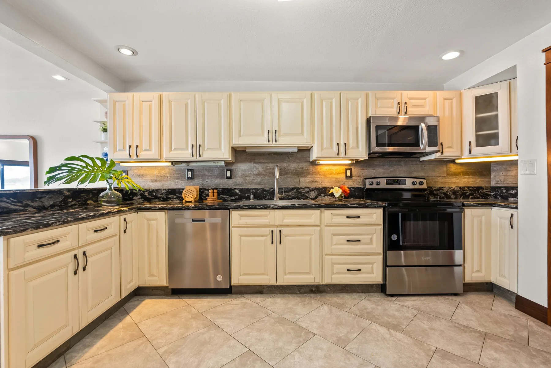 A bright kitchen with light cabinets, dark countertops, and stainless steel appliances.