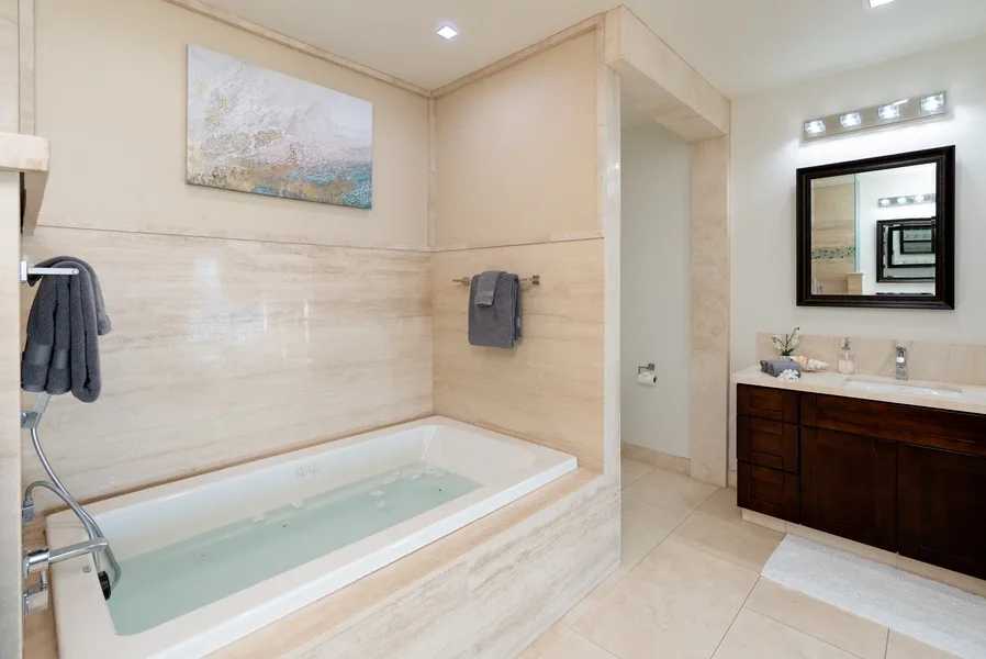A bright bathroom with a built-in bathtub and a vanity beside the mirror.