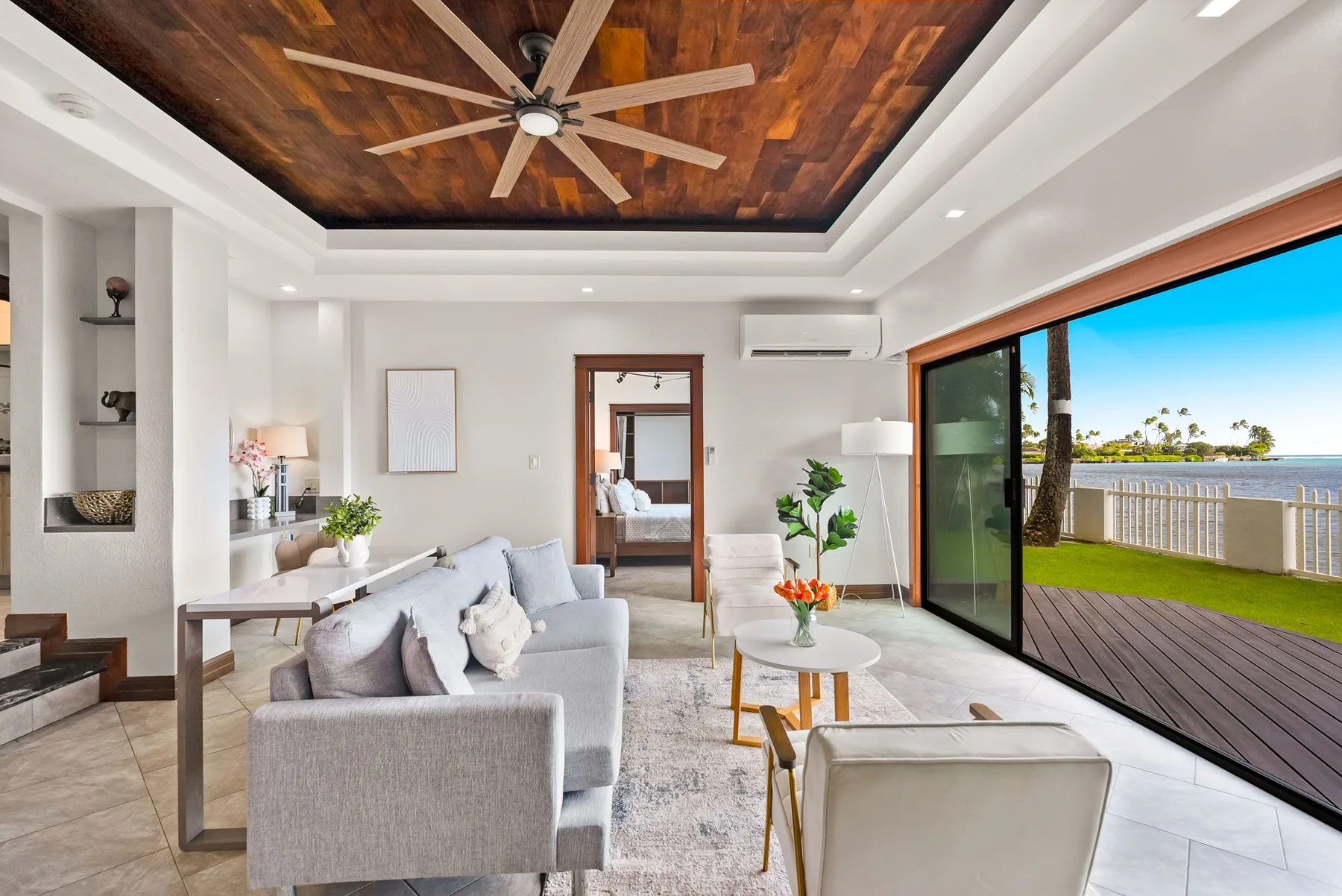 A bright living room with seating, a coffee table, and sliding glass doors opening to a lawn.