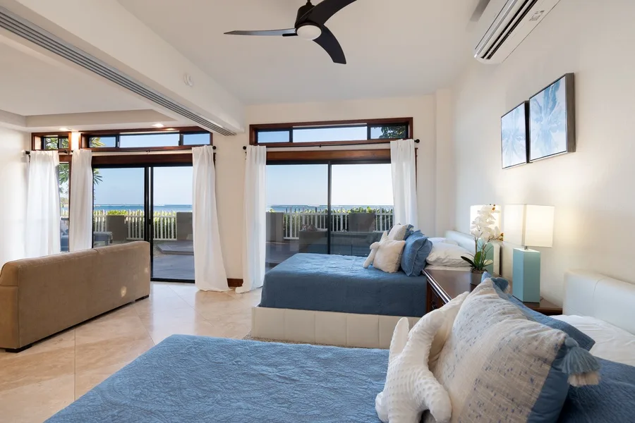 A bright bedroom with a large bed, seating, and glass doors opening to a balcony.