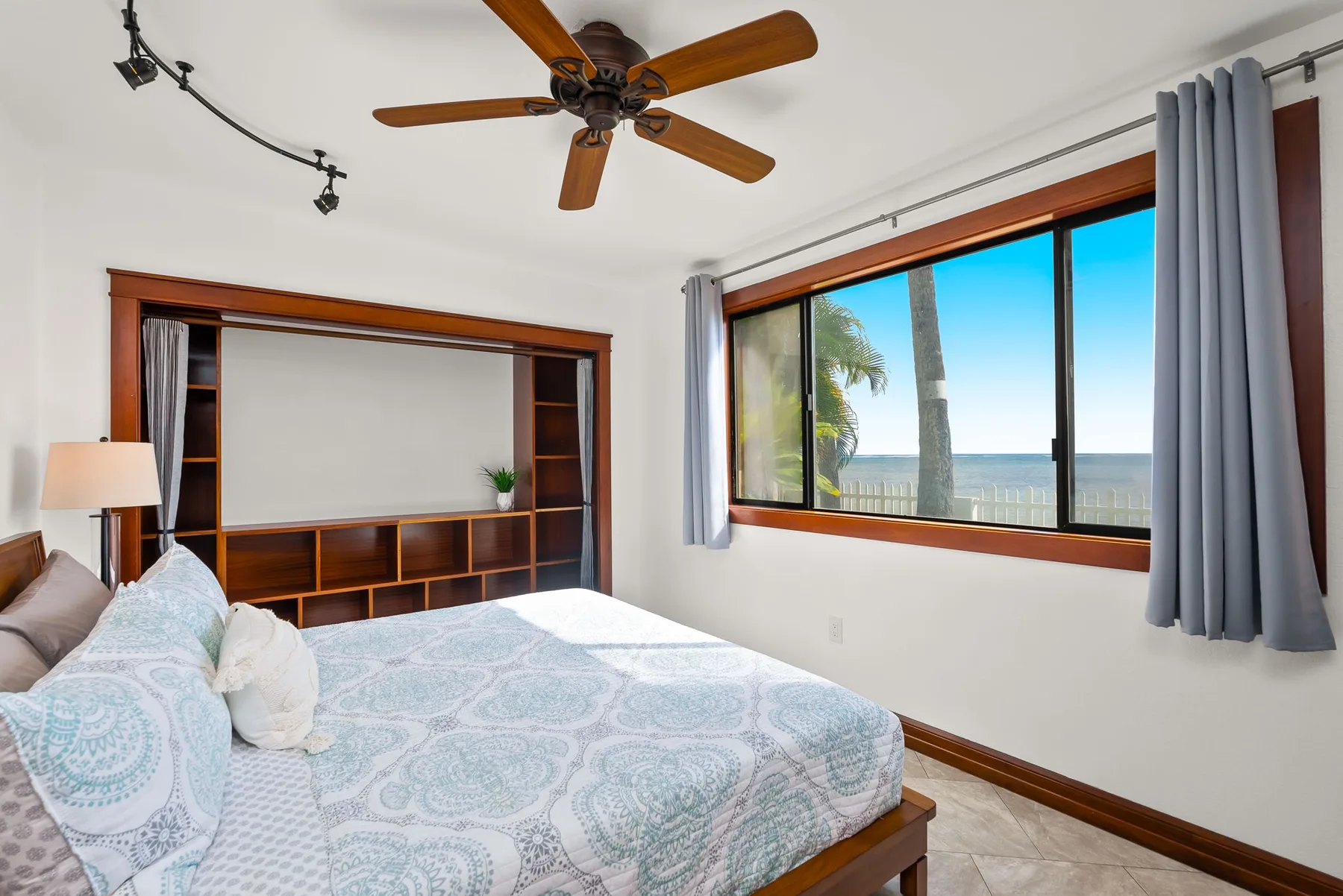 A bedroom with a bed, built-in shelving, and a large window overlooking the ocean.