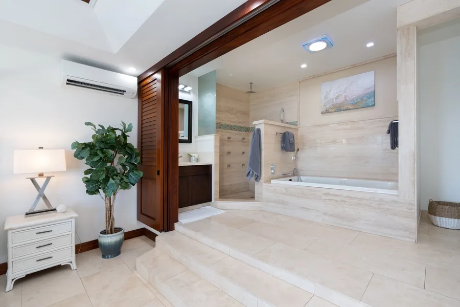 A spacious bathroom with a bathtub, pale stone surfaces, and a vanity.