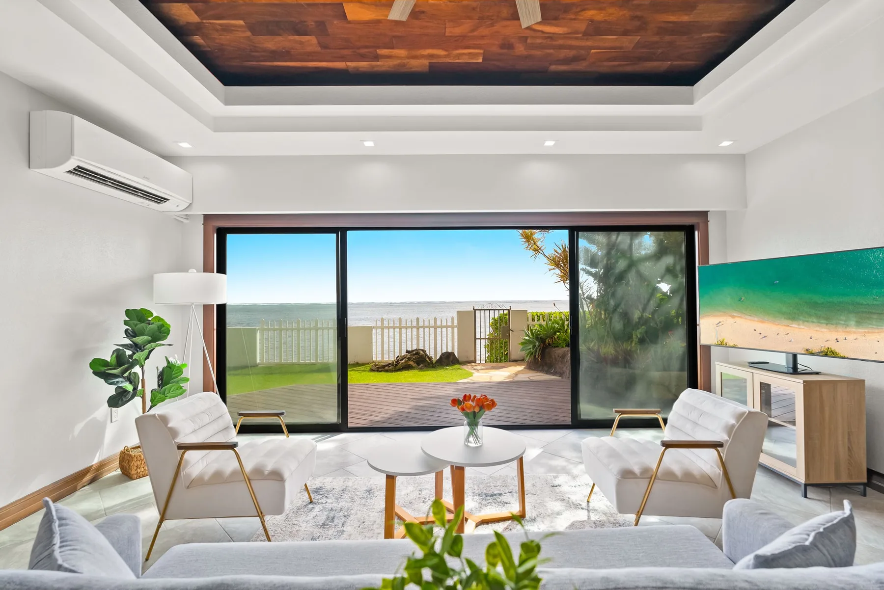 A bright living room opens through sliding glass doors to a patio and ocean view.
