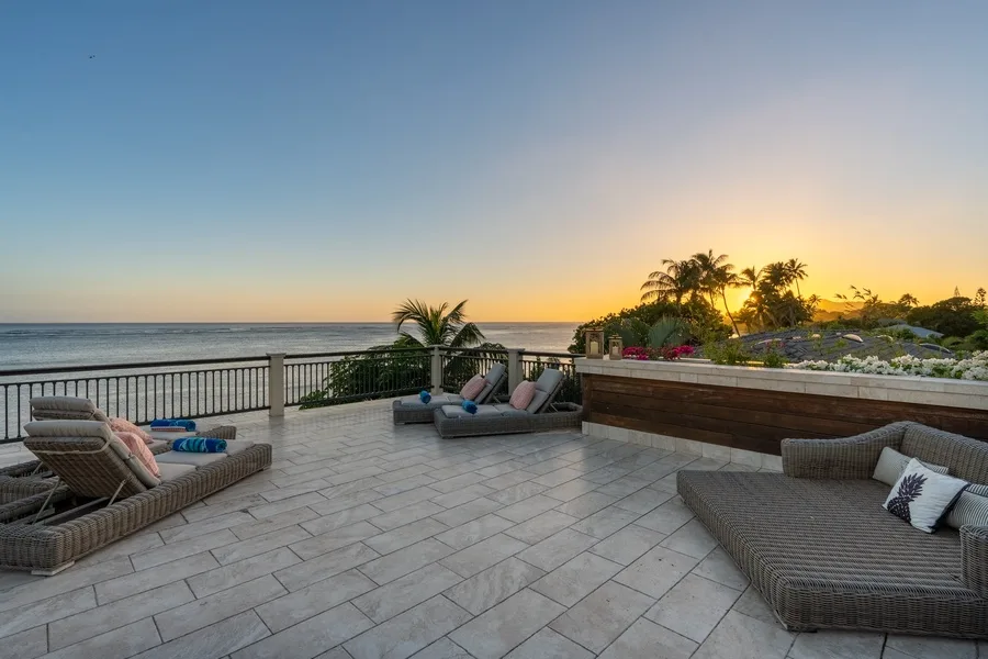 A tiled seaside terrace with lounge seating overlooks the ocean at sunset.