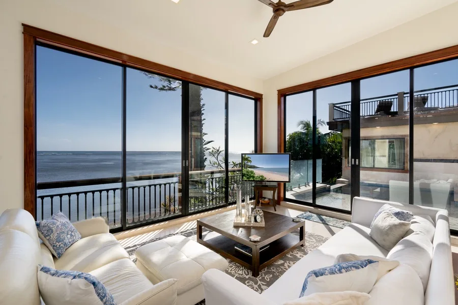 A bright living room with seating, a coffee table, and large windows overlooking the ocean.