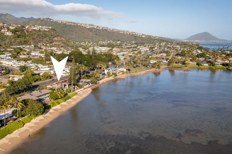 Aerial view of a coastal neighborhood beside a curved sandy shoreline and calm bay.