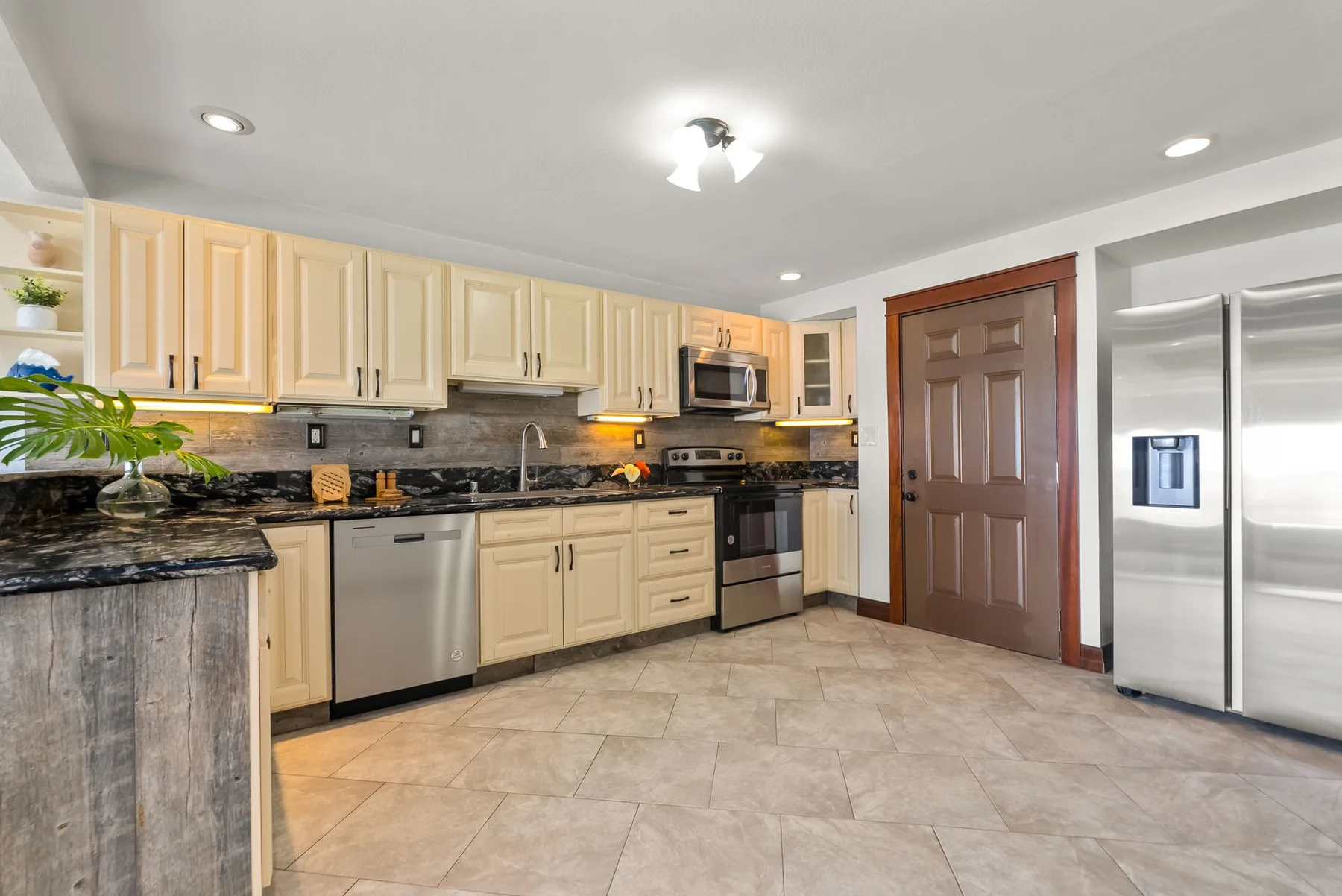 A spacious kitchen with light cabinetry, dark counters, and stainless steel appliances.