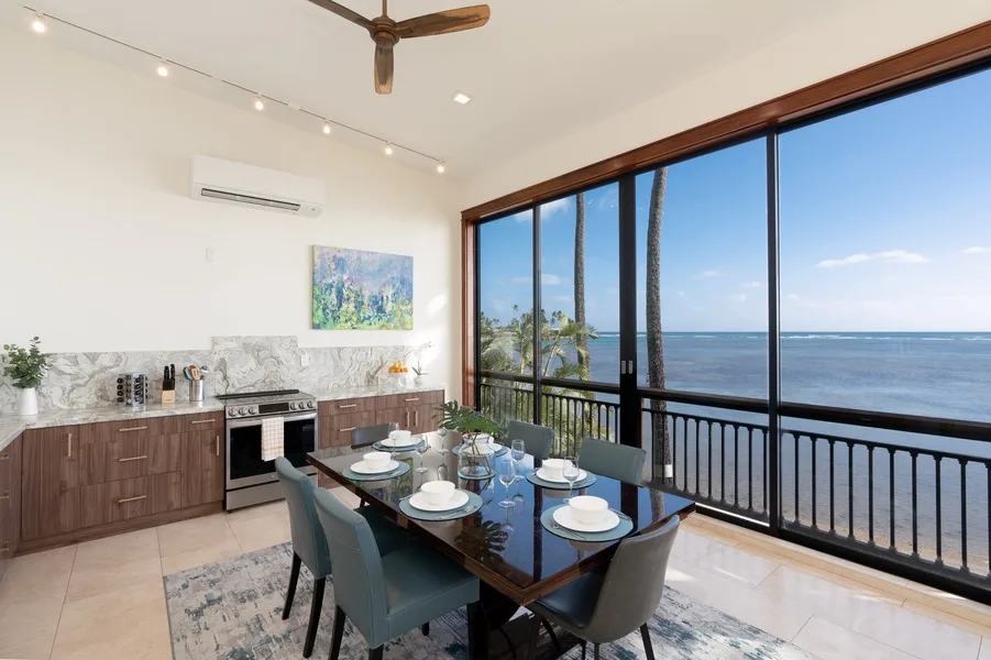 A dining area with a set table beside large windows overlooking the ocean.