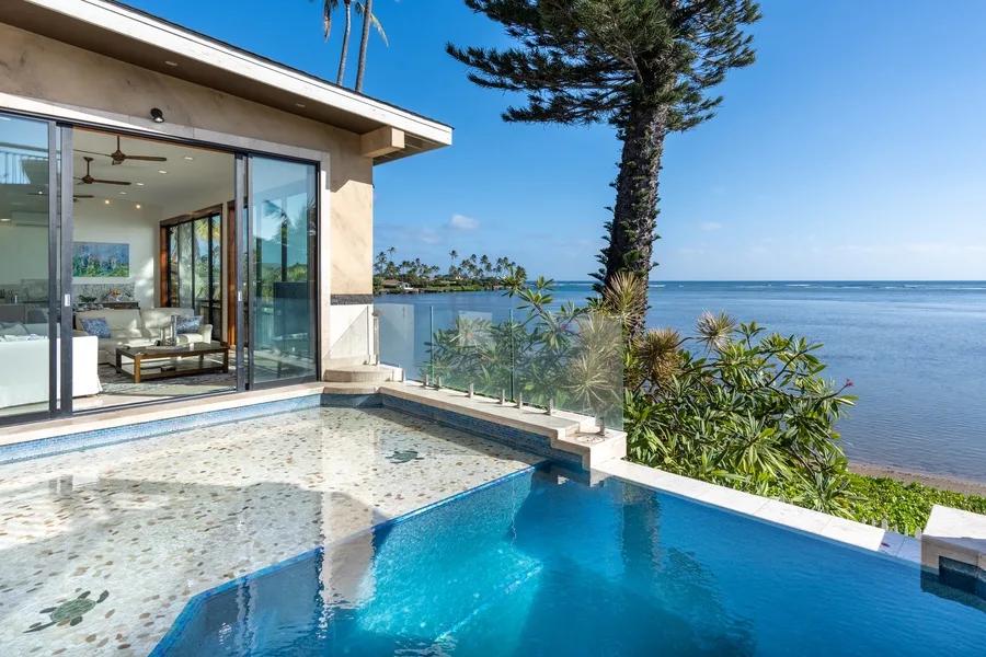 A swimming pool beside a glass-fronted house overlooks the ocean.