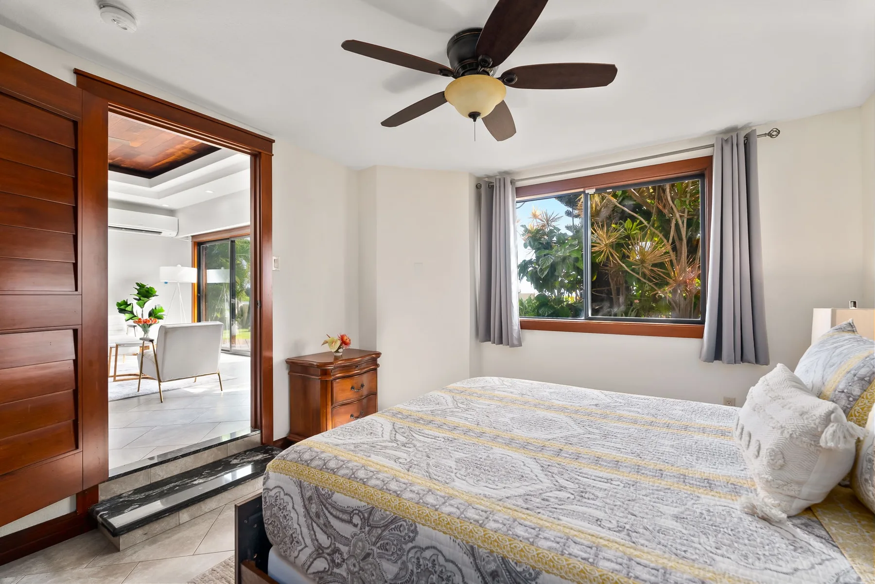 A bedroom with a bed, a ceiling fan, and a window overlooking greenery.