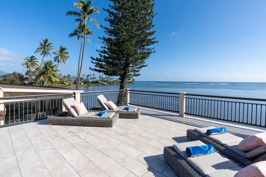 A sunlit terrace overlooks the ocean, with lounge seating beside the railing.