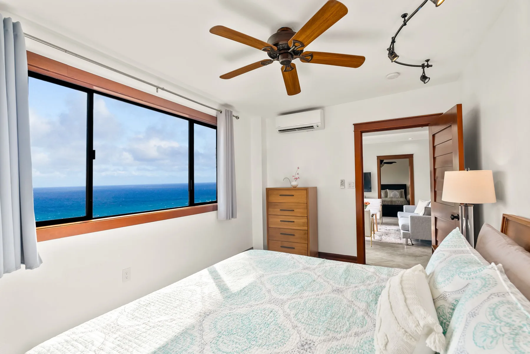 A bedroom with a large window overlooking the ocean and a bed in the foreground.