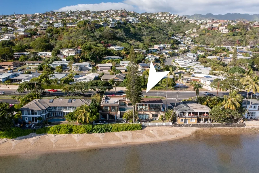A coastal neighborhood stretches behind a sandy beach, with hills in the distance.