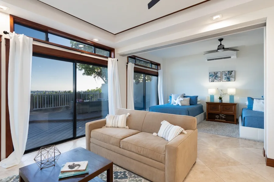 A bright living area opens onto a balcony, with seating and blue beds beyond.
