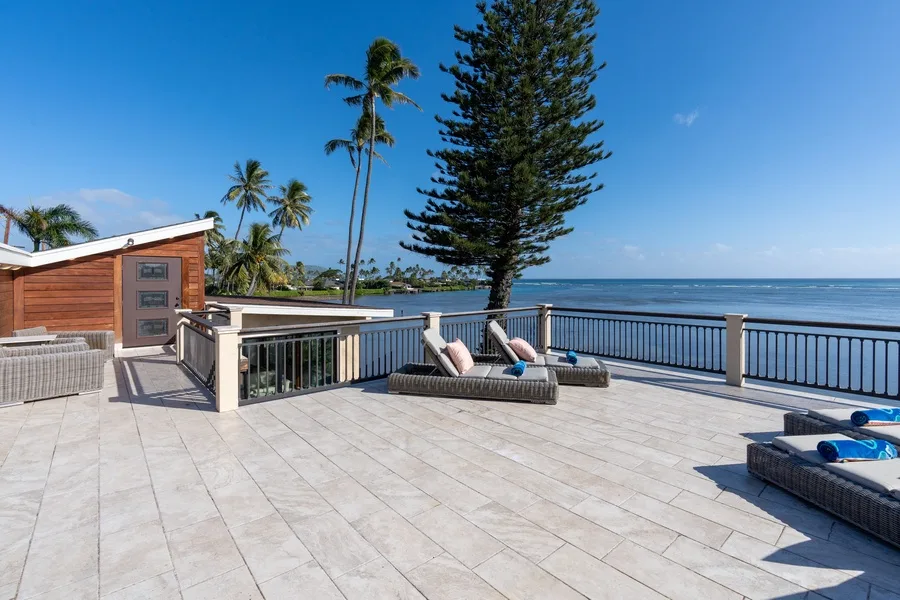 A spacious tiled terrace overlooks the ocean, with outdoor seating by the railing.